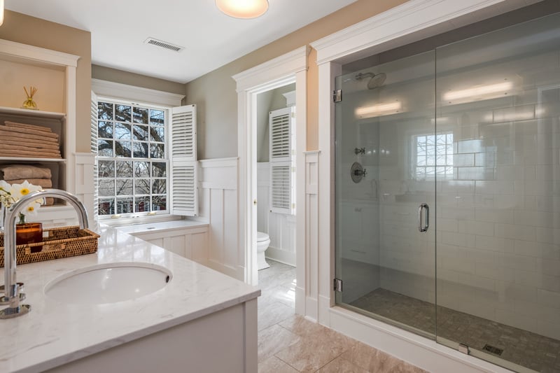 The primary bath features tile shower, plantation shutters and charming wainscotting.